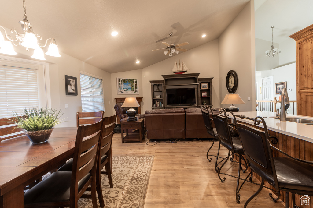 Dining space with light hardwood / wood-style flooring, sink, ceiling fan with notable chandelier, and high vaulted ceiling