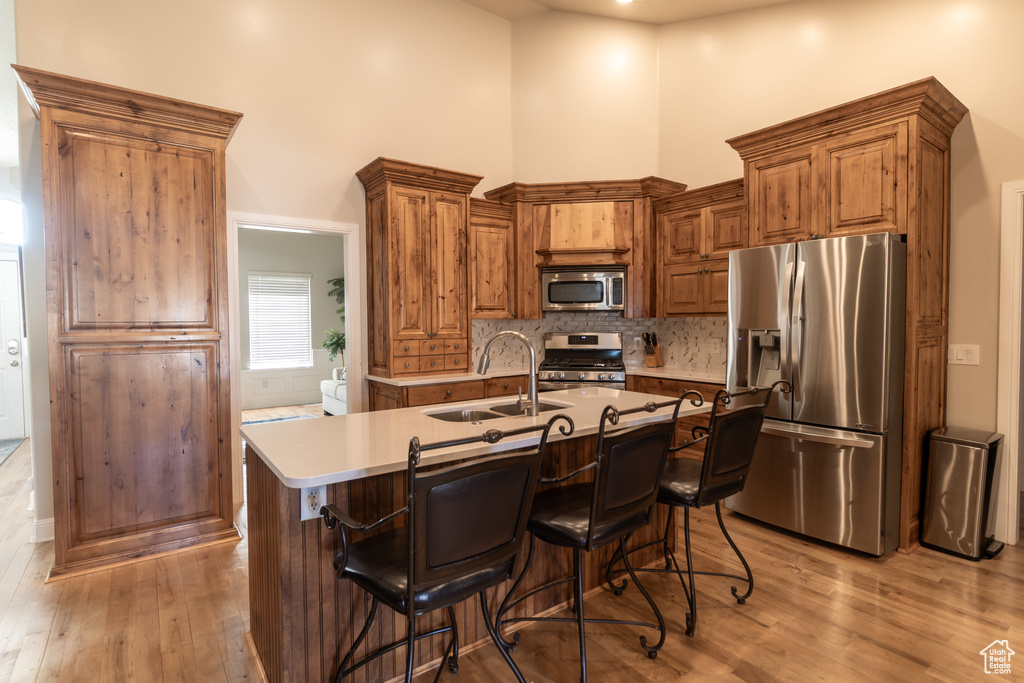 Kitchen featuring light hardwood / wood-style flooring, appliances with stainless steel finishes, sink, a breakfast bar area, and a kitchen island with sink