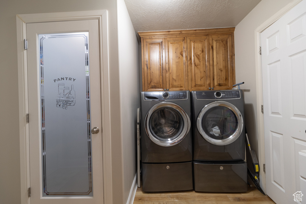 Laundry area with independent washer and dryer, light hardwood / wood-style floors, cabinets, and a textured ceiling