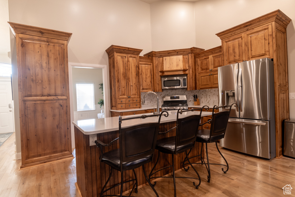 Kitchen featuring appliances with stainless steel finishes, light hardwood / wood-style floors, a breakfast bar, a kitchen island, and a towering ceiling