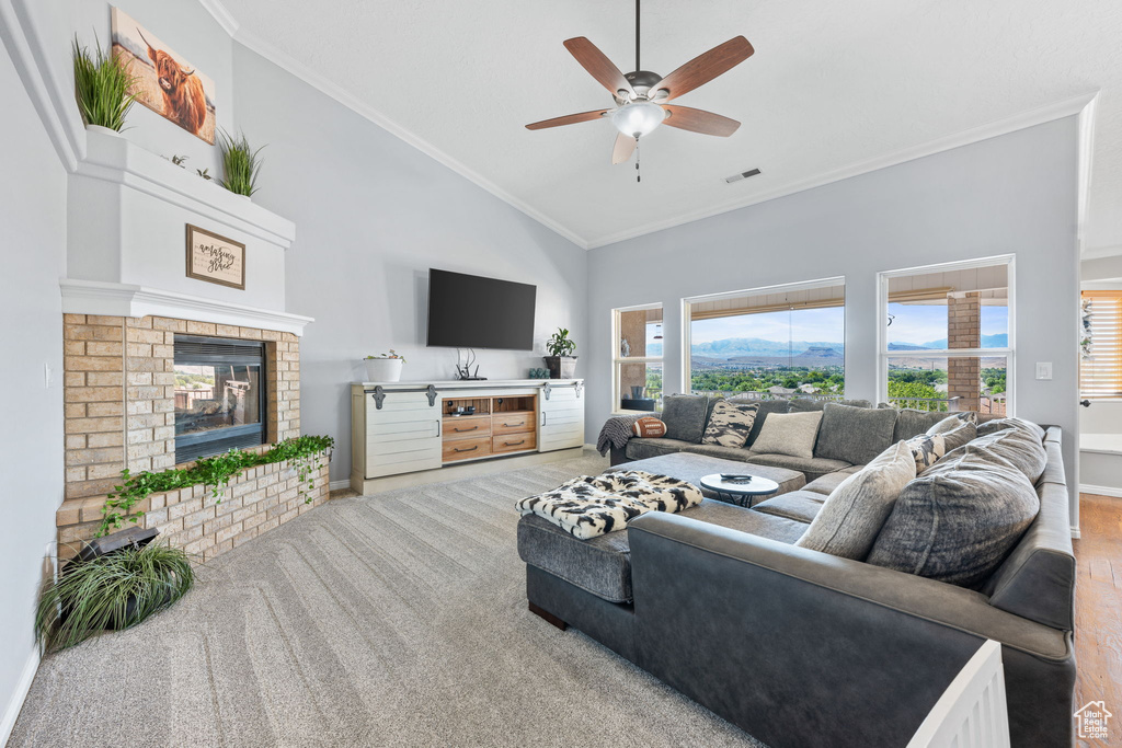 Carpeted living room featuring crown molding, ceiling fan, high vaulted ceiling, and a fireplace