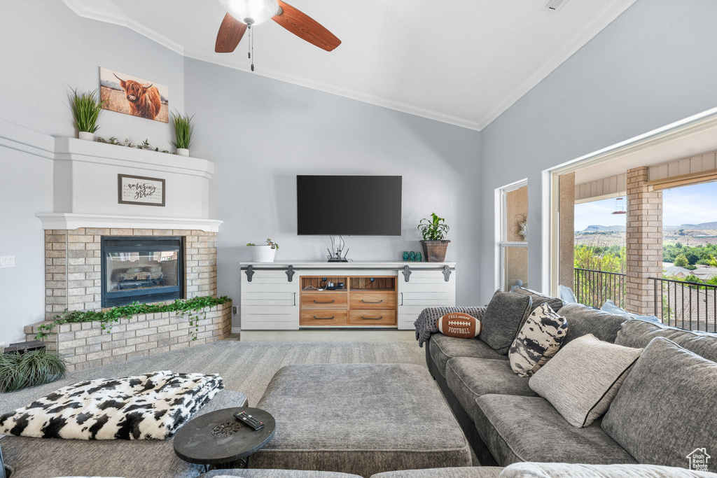 Carpeted living room with a fireplace, crown molding, high vaulted ceiling, and ceiling fan