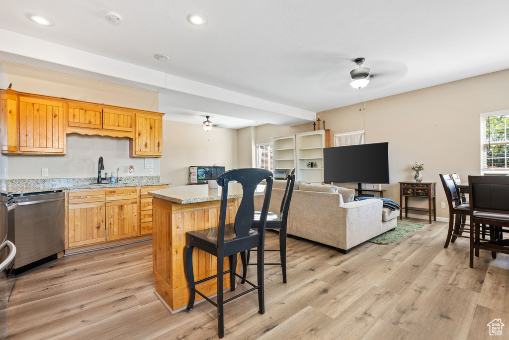 Kitchen featuring a center island, light wood-type flooring, light stone countertops, ceiling fan, and stainless steel dishwasher