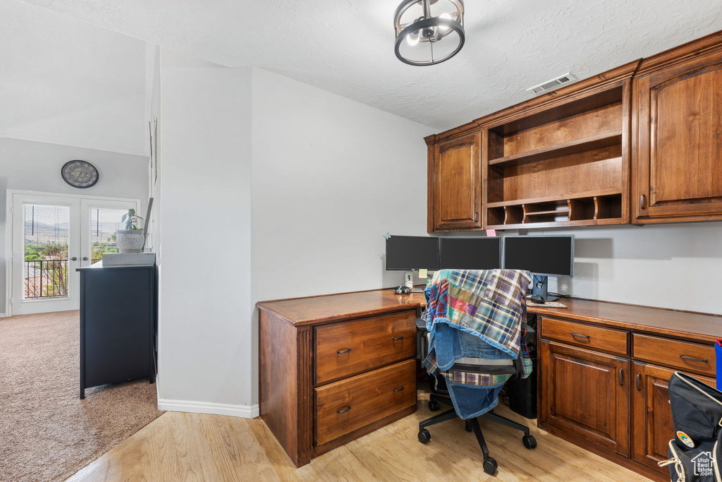 Home office featuring built in desk, a textured ceiling, and light hardwood / wood-style flooring