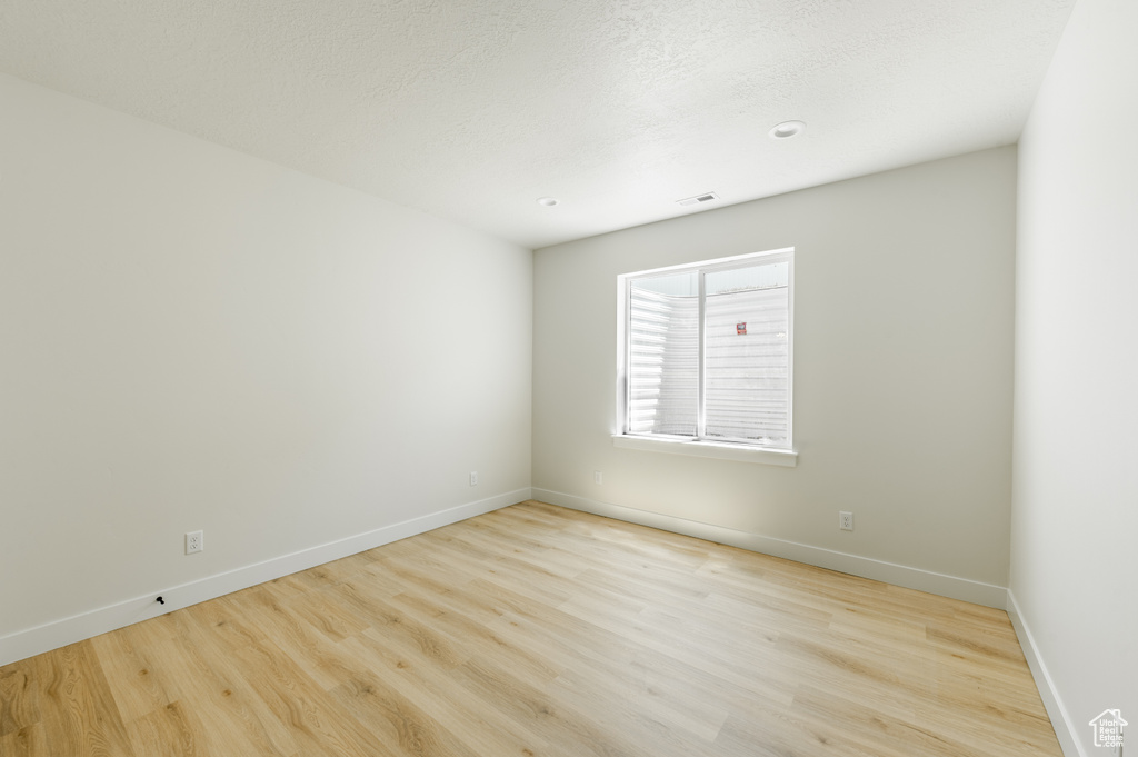 Empty room with a textured ceiling and light hardwood / wood-style flooring