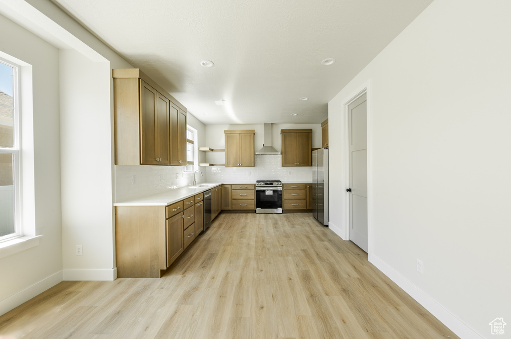 Kitchen with stainless steel appliances, tasteful backsplash, wall chimney exhaust hood, and light hardwood / wood-style floors