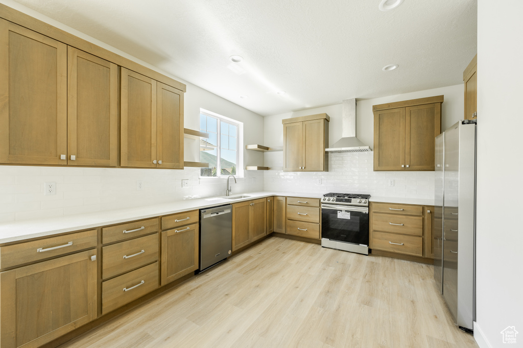 Kitchen featuring light hardwood / wood-style flooring, backsplash, stainless steel appliances, sink, and wall chimney range hood