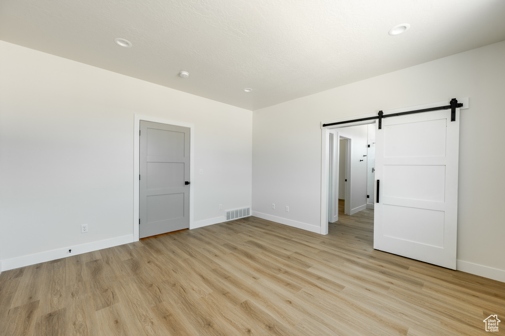 Unfurnished room with a barn door and light hardwood / wood-style floors