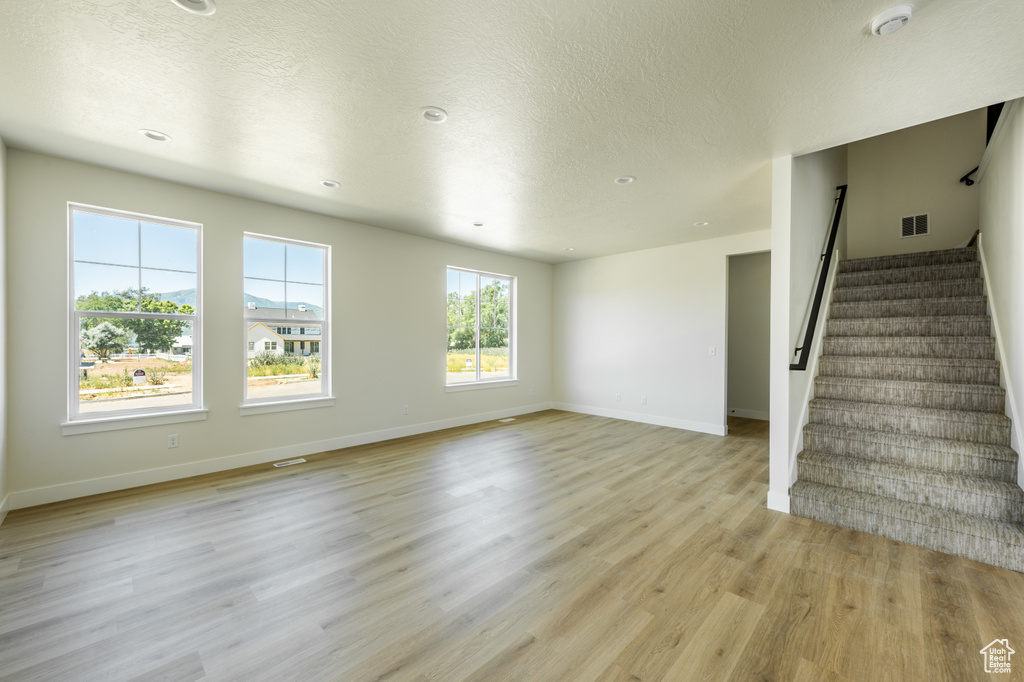 Unfurnished living room with a wealth of natural light, light hardwood / wood-style flooring, and a textured ceiling