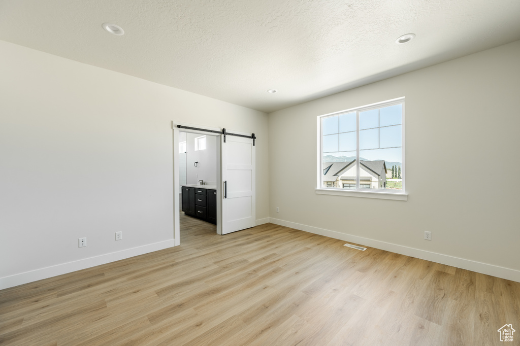 Unfurnished bedroom featuring a barn door, light wood-type flooring, and a textured ceiling