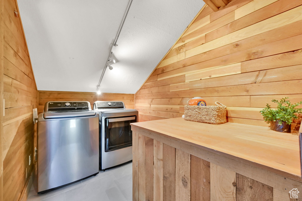 Washroom with washing machine and dryer, wooden walls, and track lighting