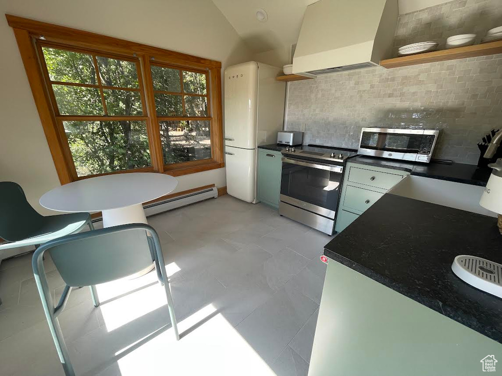 Kitchen featuring custom exhaust hood, vaulted ceiling, stainless steel appliances, decorative backsplash, and baseboard heating