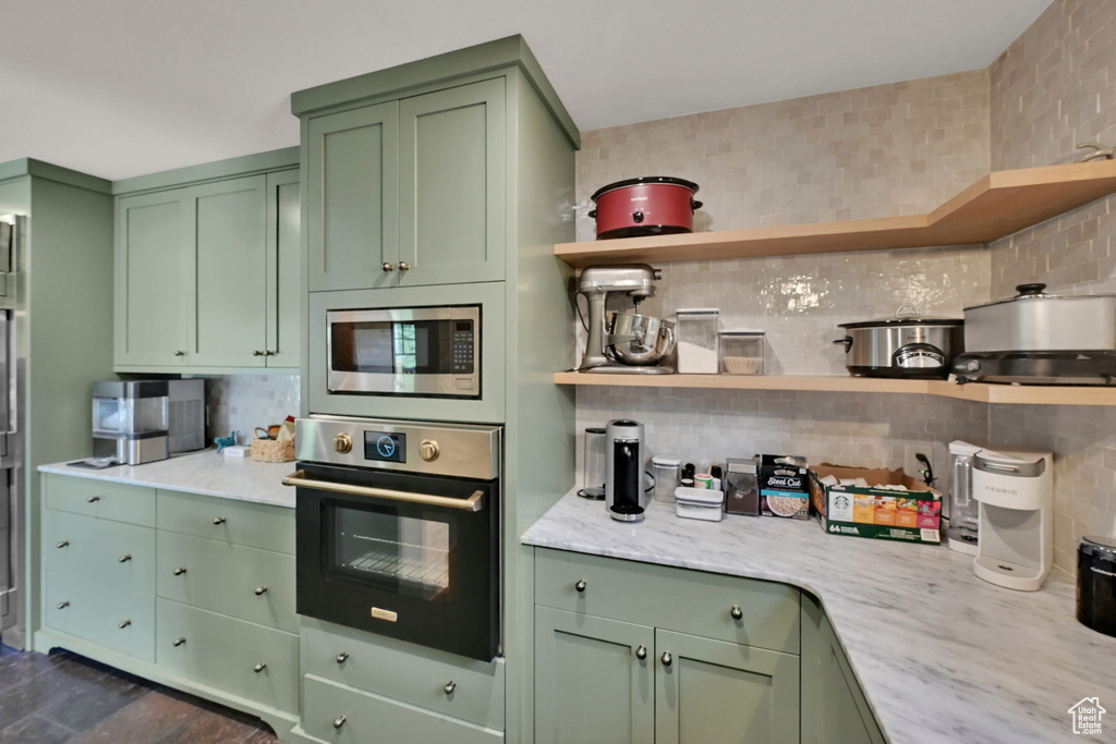 Kitchen with light stone counters, appliances with stainless steel finishes, green cabinets, and tasteful backsplash