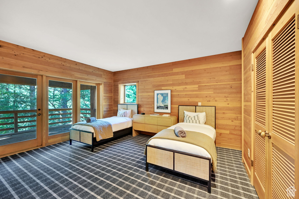 Bedroom with dark carpet, wood walls, and access to outside