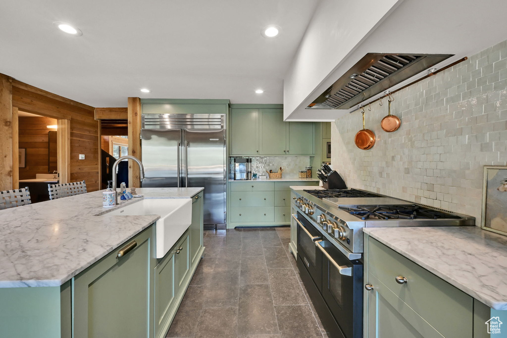 Kitchen featuring green cabinetry, an island with sink, sink, and premium appliances