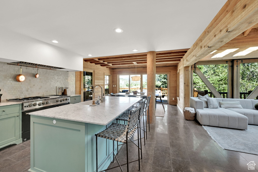 Kitchen featuring hanging light fixtures, light stone counters, high end stove, sink, and a center island with sink