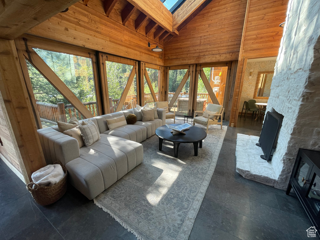 Tiled living room with high vaulted ceiling, a wealth of natural light, beamed ceiling, and a stone fireplace