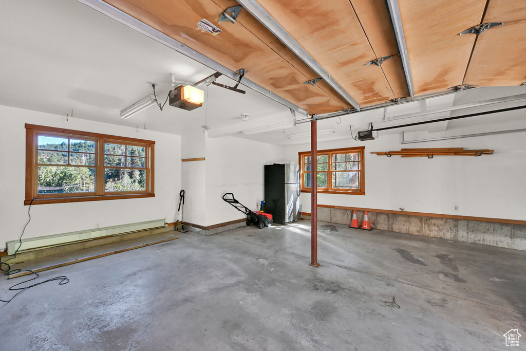 Garage with a baseboard heating unit, stainless steel fridge, and a garage door opener