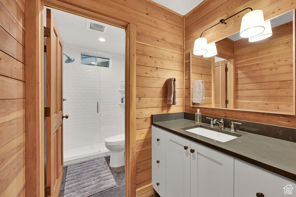 Bathroom with vanity, toilet, a shower with shower door, and wood walls