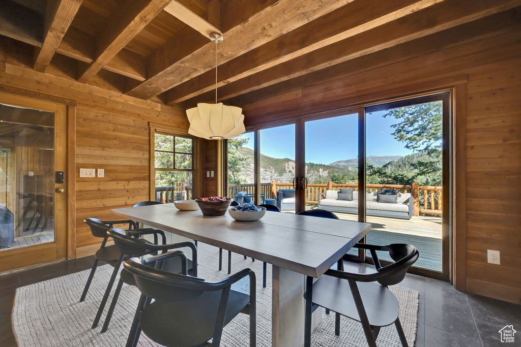 Dining area with a wealth of natural light, a mountain view, wood walls, and beam ceiling