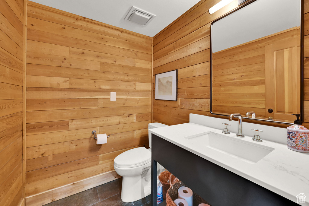 Bathroom featuring vanity, toilet, wood walls, and tile patterned flooring