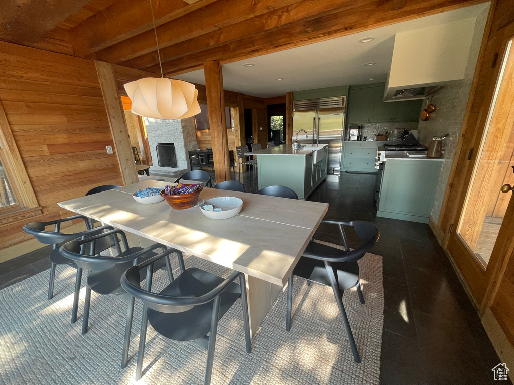 Tiled dining area featuring sink, wood walls, beamed ceiling, and a fireplace