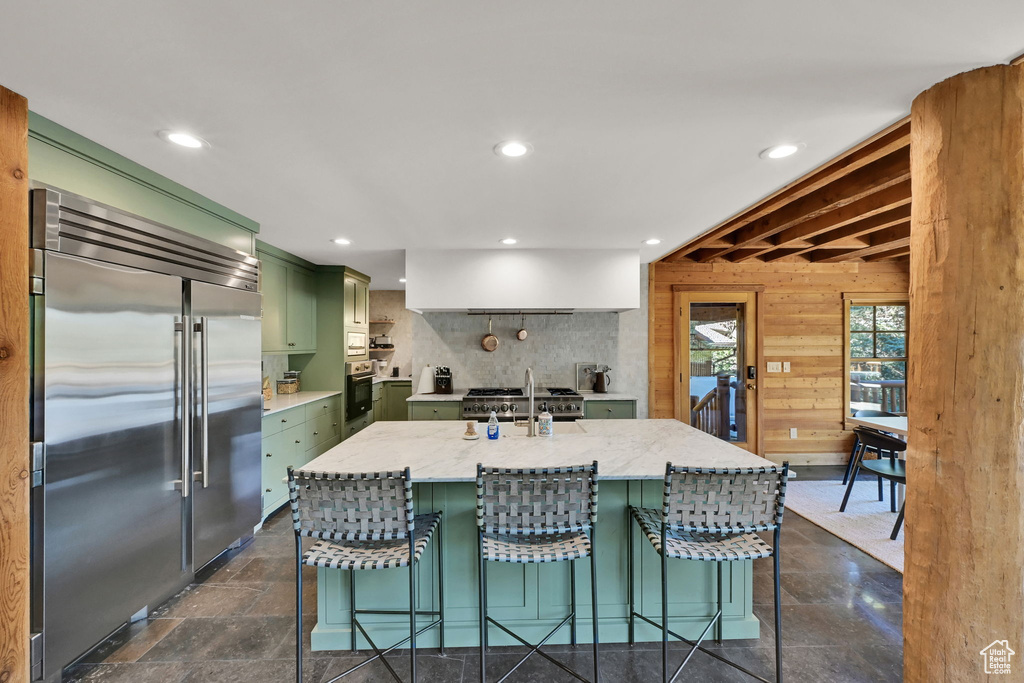 Kitchen with a kitchen island with sink, green cabinets, wood walls, light stone countertops, and premium appliances