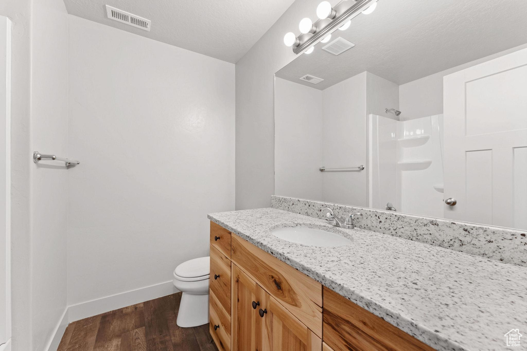 Bathroom featuring hardwood / wood-style flooring, walk in shower, toilet, vanity, and a textured ceiling