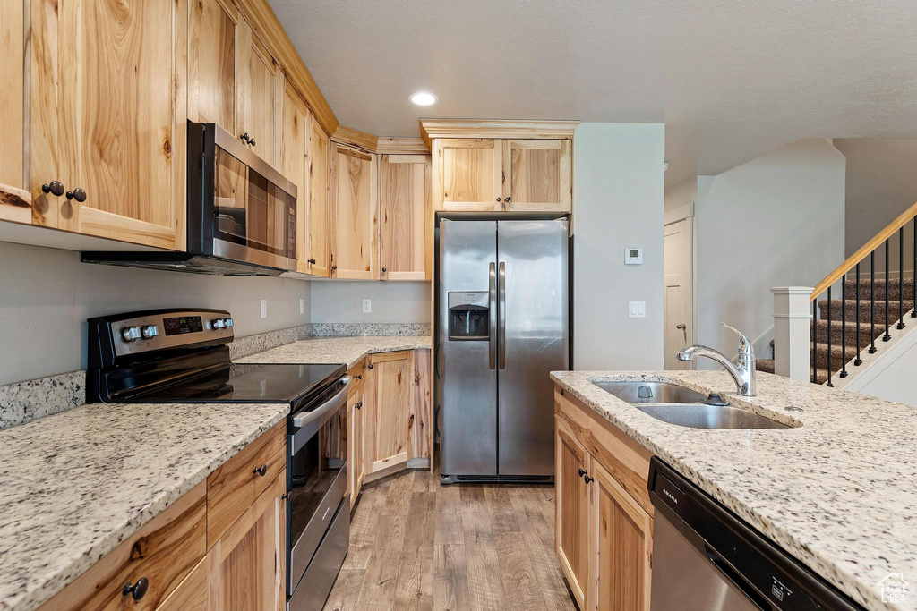 Kitchen featuring appliances with stainless steel finishes, light hardwood / wood-style flooring, light stone counters, and sink