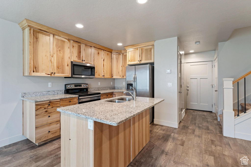 Kitchen featuring light stone countertops, stainless steel appliances, sink, dark hardwood / wood-style floors, and an island with sink