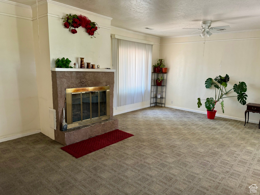 Unfurnished living room with crown molding, carpet flooring, a premium fireplace, ceiling fan, and a textured ceiling