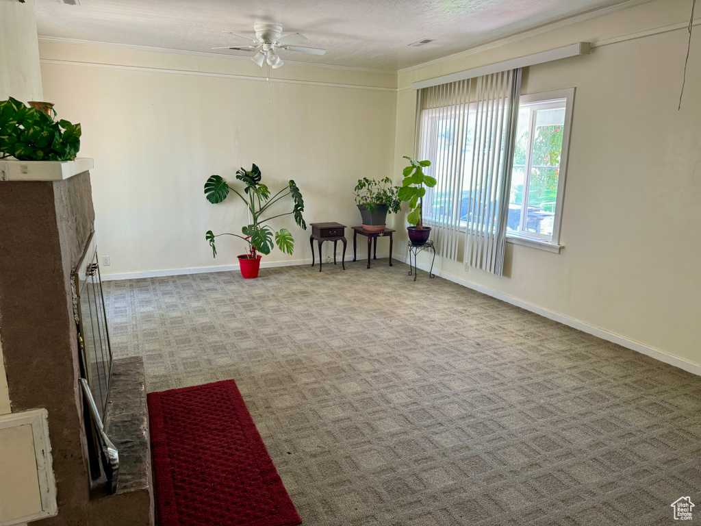 Living area featuring ceiling fan, light colored carpet, a fireplace, and ornamental molding