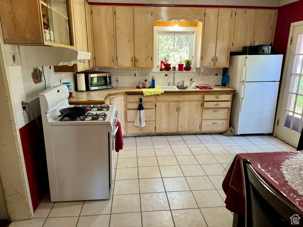 Kitchen with white appliances, a healthy amount of sunlight, light tile patterned floors, and decorative backsplash