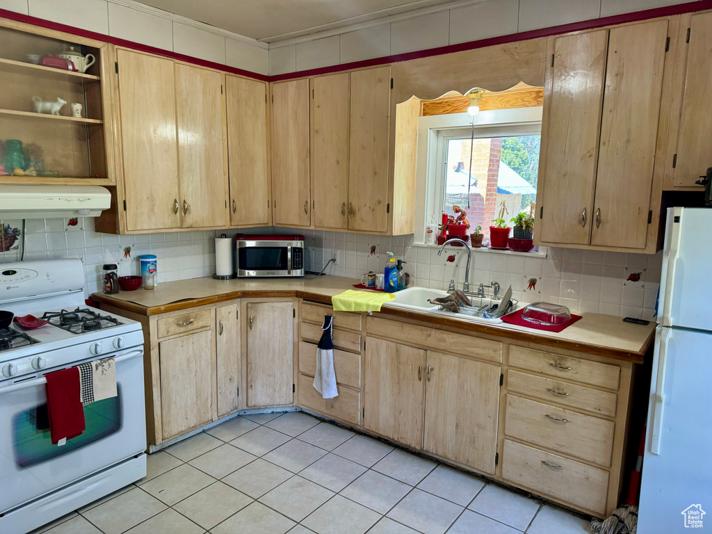 Kitchen with white appliances, light brown cabinetry, light tile patterned floors, backsplash, and sink