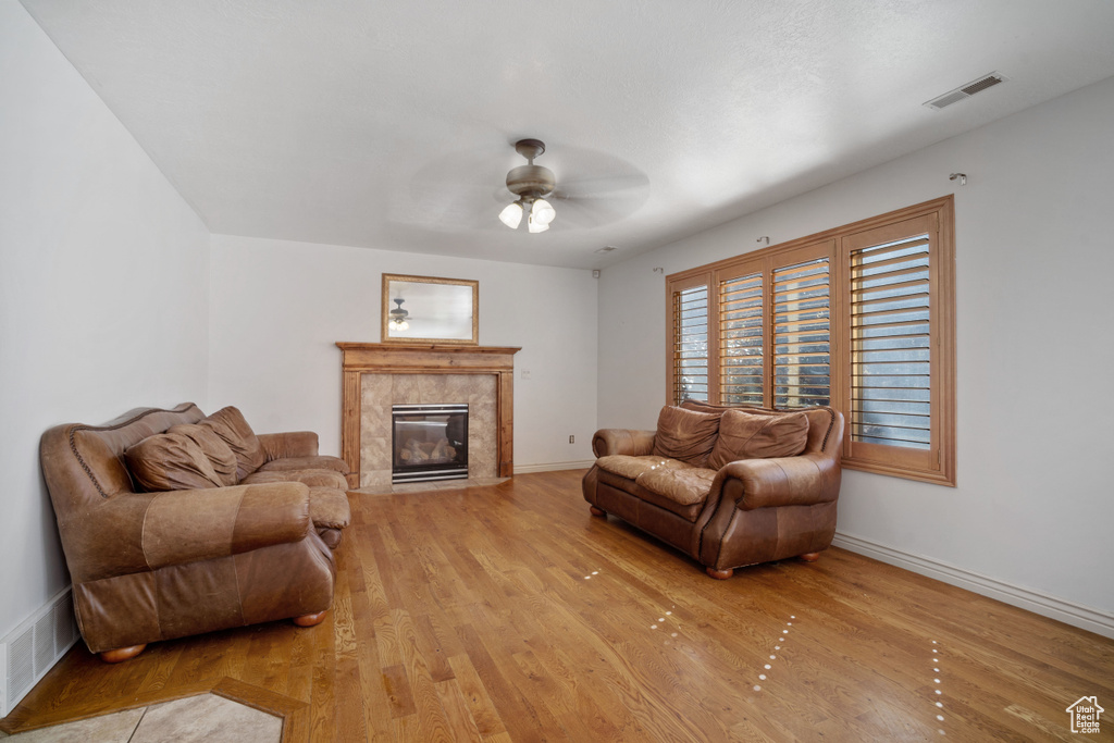 Living room with a fireplace, ceiling fan, and light hardwood / wood-style floors