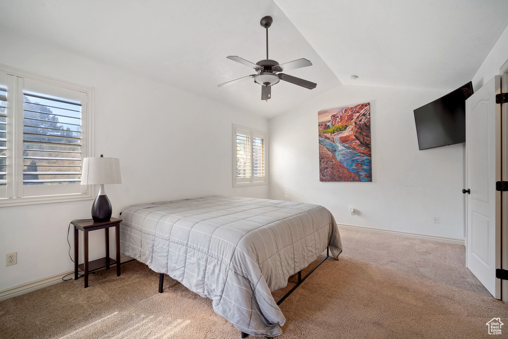 Carpeted bedroom featuring multiple windows, vaulted ceiling, and ceiling fan