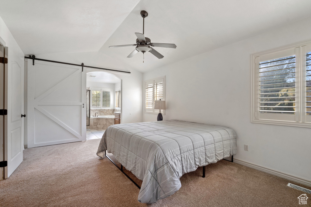 Carpeted bedroom featuring a barn door, ceiling fan, vaulted ceiling, and connected bathroom