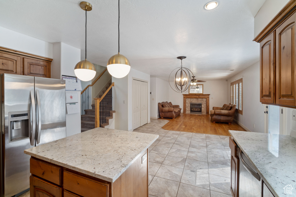 Kitchen featuring light tile patterned floors, decorative light fixtures, appliances with stainless steel finishes, light stone counters, and a kitchen island