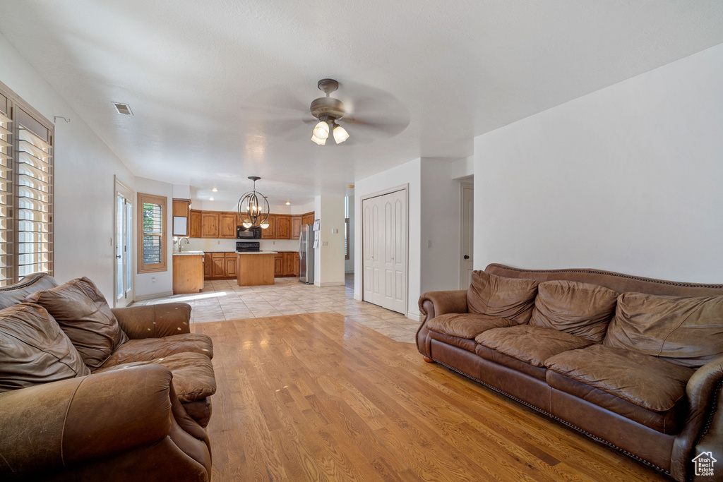 Living room featuring ceiling fan with notable chandelier, light hardwood / wood-style flooring, and sink