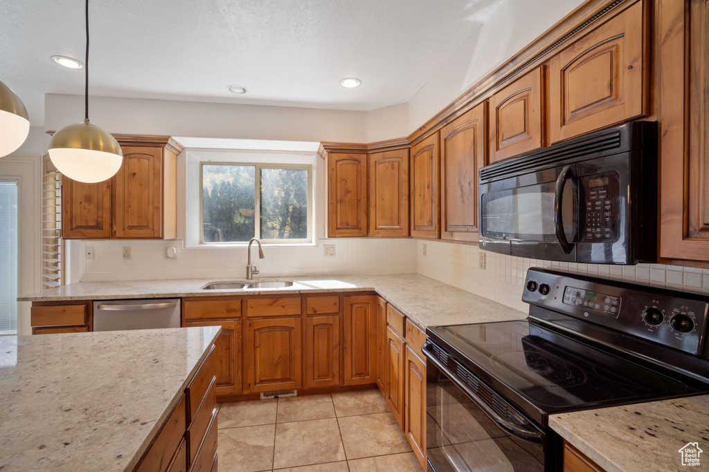 Kitchen with black appliances, hanging light fixtures, light stone countertops, and sink