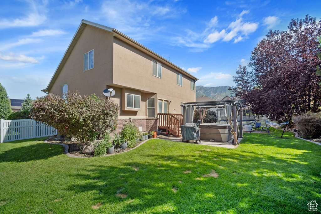 Back of house with a hot tub and a yard