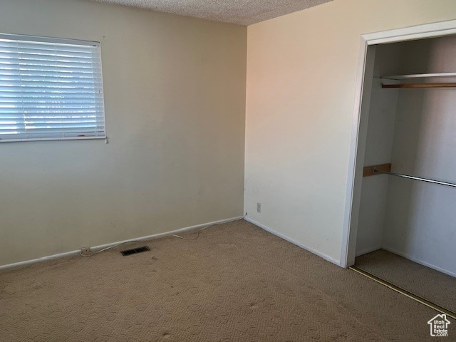 Unfurnished bedroom with a closet, light carpet, and a textured ceiling