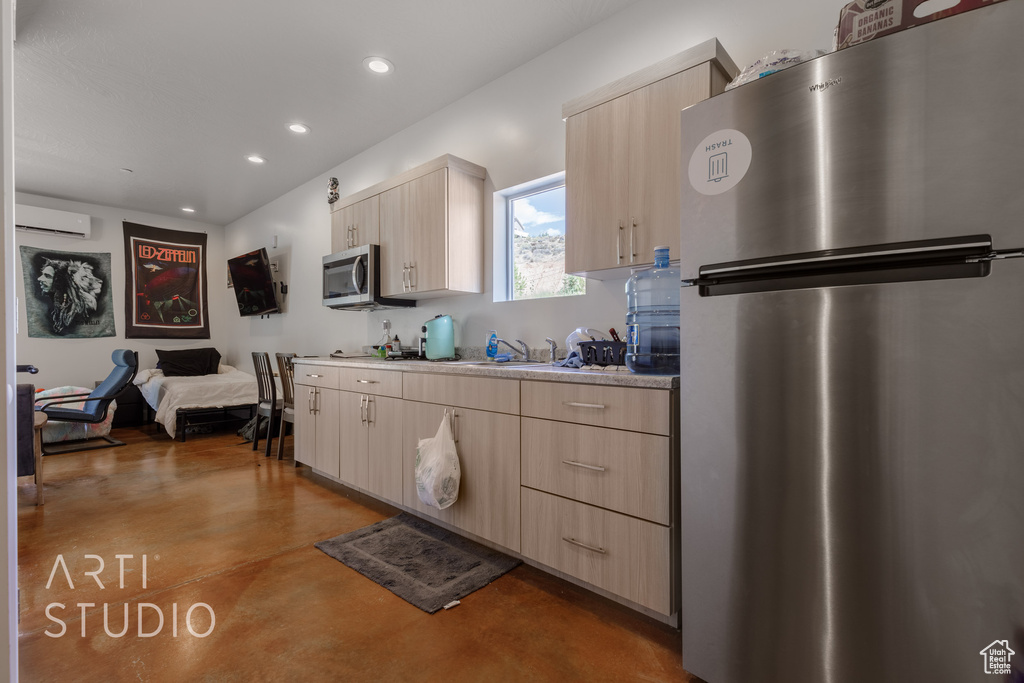 Kitchen with an AC wall unit, light brown cabinetry, and appliances with stainless steel finishes