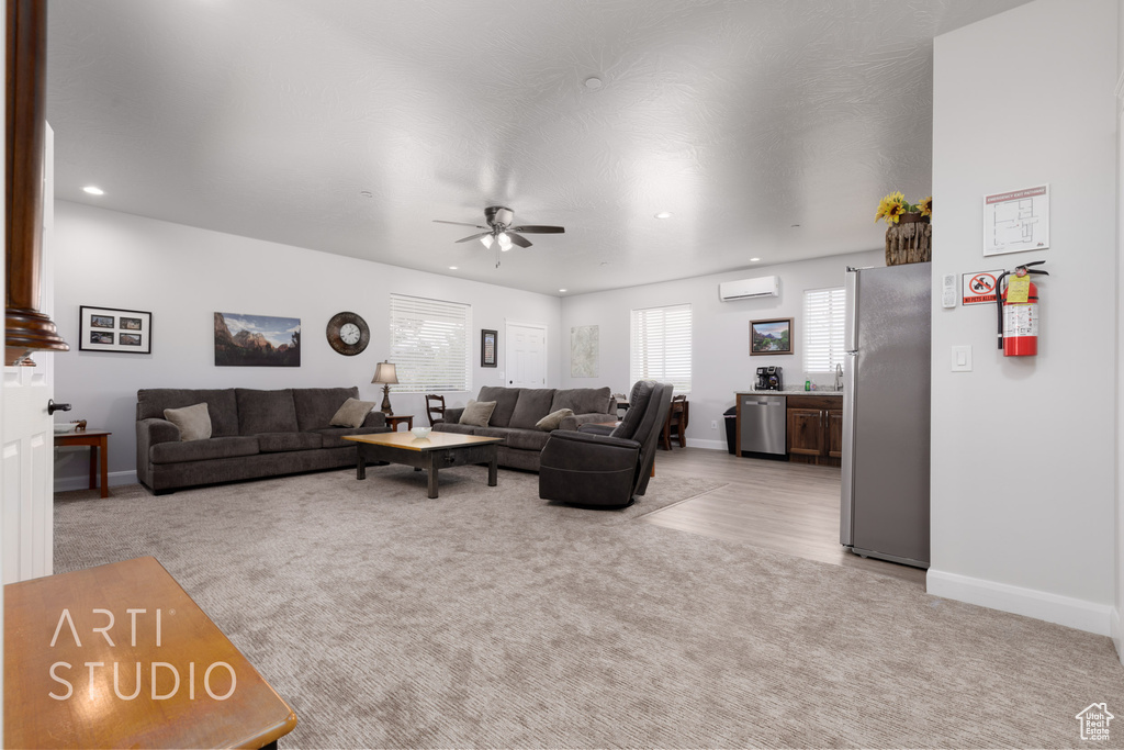 Living room featuring ceiling fan, light colored carpet, and a wall mounted air conditioner