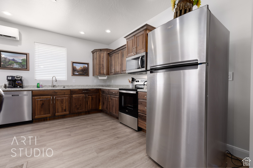 Kitchen with sink, appliances with stainless steel finishes, a wall mounted AC, light stone countertops, and light hardwood / wood-style floors