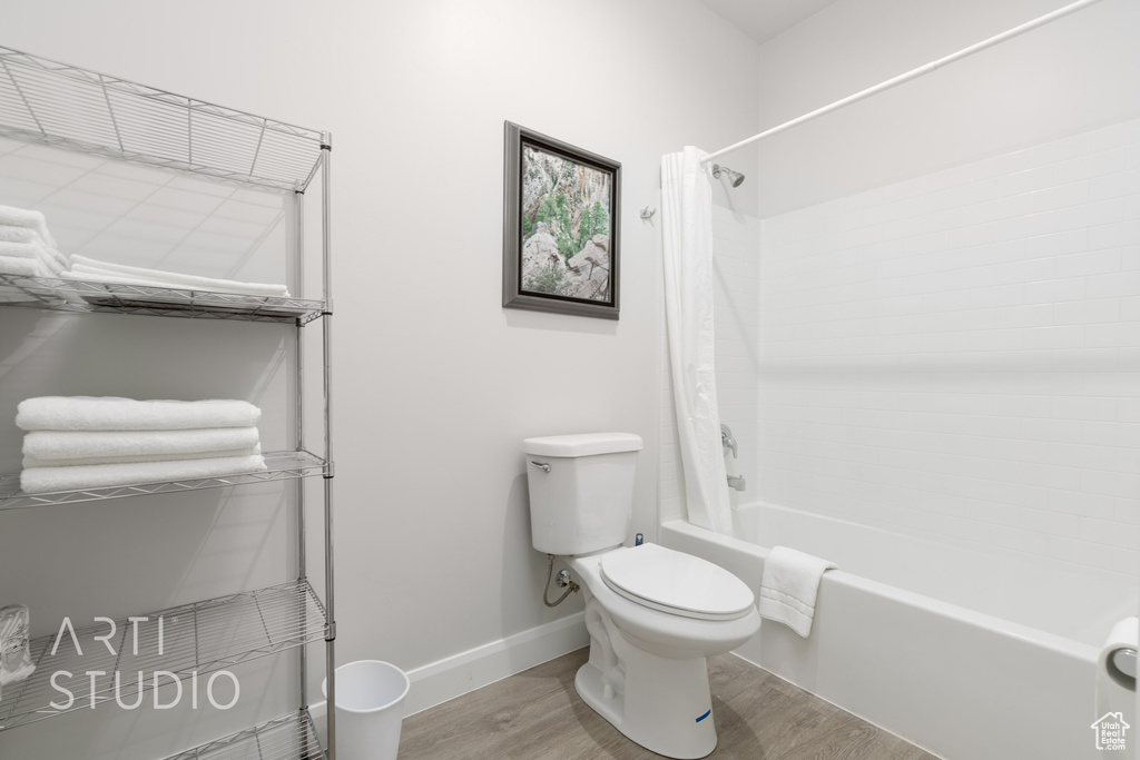 Bathroom with shower / bathtub combination with curtain, hardwood / wood-style floors, and toilet