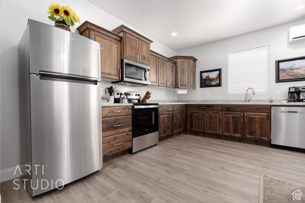 Kitchen featuring sink, stainless steel appliances, light hardwood / wood-style flooring, and light stone countertops