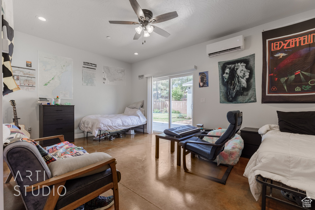 Bedroom featuring ceiling fan, concrete flooring, a wall unit AC, and access to exterior