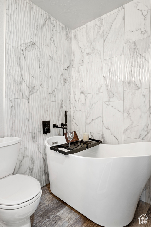 Bathroom with a tub to relax in, tile walls, toilet, and hardwood / wood-style flooring