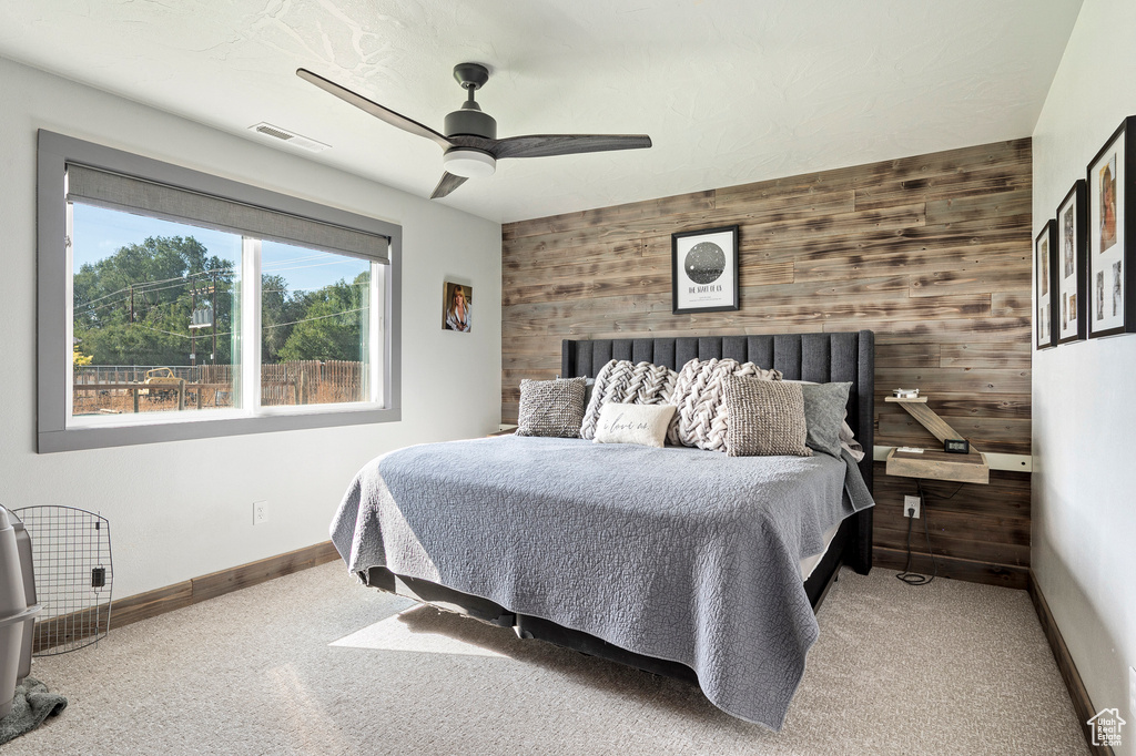 Bedroom with carpet flooring, wood walls, and ceiling fan